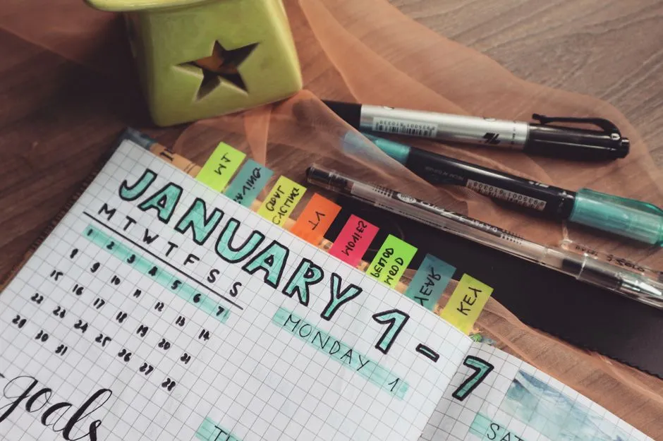 Paper planner, pen, and desk calendar used for laying out a printed monthly schedule